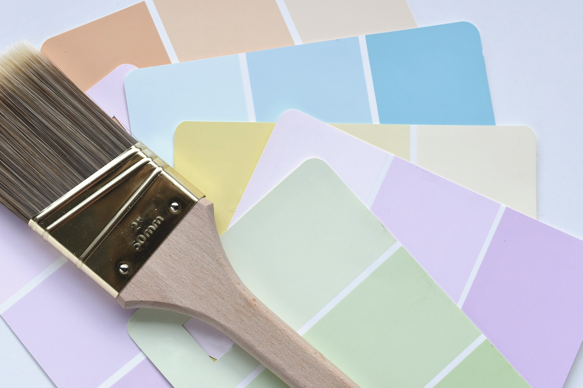 Muted light pastel paint color samples with a paintbrush.